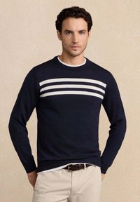 Maglione navy a girocollo con strisce orizzontali bianche sul petto, texture a maglia e maniche lunghe, indossato sopra una maglietta bianca.