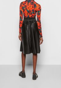 Person som bär en svart läderkjol med elastisk midja och stora bakfickor, en färgglad röd och svart mönstrad långärmad tröja och svarta skor.