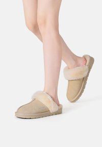 Beige Wildlederschuhe mit einem flauschigen Kunstfellkragen, runder Zehenform und strukturiertem Gummisohlendesign für Komfort und Wärme.
