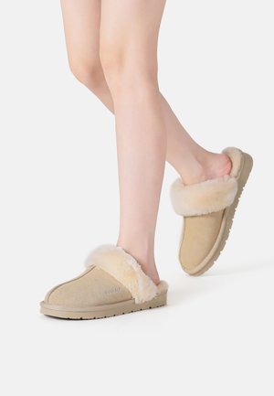 Beige suede slippers with a fluffy faux fur collar, rounded toe shape, and textured rubber sole, designed for comfort and warmth.