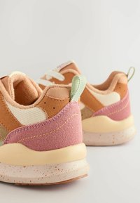Sneakers w połączeniu jasnobrązowego, kremowego i różowego zamszu; charakteryzują się teksturowaną powierzchnią i cętkowaną podeszwą z miętowozieloną pętelką na pięcie.