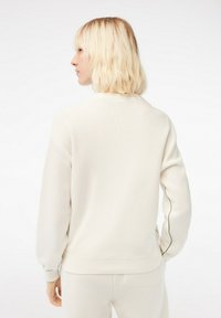 Crèmekleurige trui met ribbelstructuur, verlaagde schouderontwerp en contrasterende groene stiksels langs de mouwen en op de rug.
