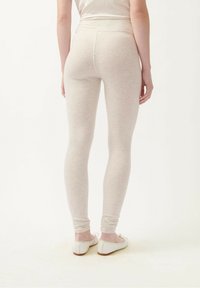 Šviesiai béžinės leginsai su glotnia tekstūra, aukštu liemeniu ir slim fit siluetu, derinami su paprastais baltais butų tipo batais.