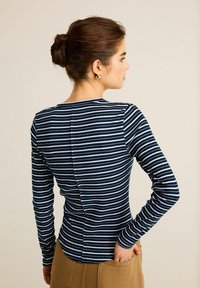 Pitkähihainen, tummansinivalkoinen raidallinen paita, jossa on pyöreä kaula-aukko ja takasauman yksityiskohta. Pehmeä, teksturoitu kangas ja slim fit -mielle.