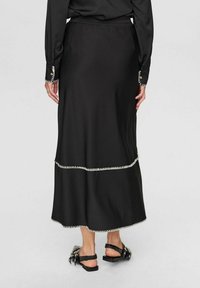 Černá sukně s vrstveným designem; okraje s vlnkovým lemem a bílým stehem. Elastický pas, hladká textura a délka po kotníky. Kombinováno s černými sandály.