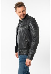Schwarze Lederjacke mit Reißverschlusstaschen, gesteppte Schulterakzente und Druckknopfkragen, gestaltet mit einer taillierten Passform und glatter Textur.