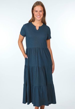 T-Shirt-Kleid in Dunkelblau mit V-Ausschnitt, kurzen Ärmeln und gestuften Rüschensaum. Hergestellt aus weichem, strukturiertem Stoff mit seitlichen Taschen.
