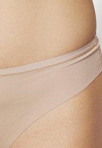 Culottes de bikini beiges en tissu lisse et extensible avec une taille basse, présentant des coutures plates et une finition sans coutures pour le confort.
