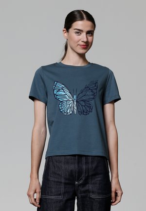 Turkoois katoenen T-shirt met een vlinderafbeelding in tinten blauw en zwart. Korte mouwen, ronde halslijn, losse pasvorm, gladde textuur.