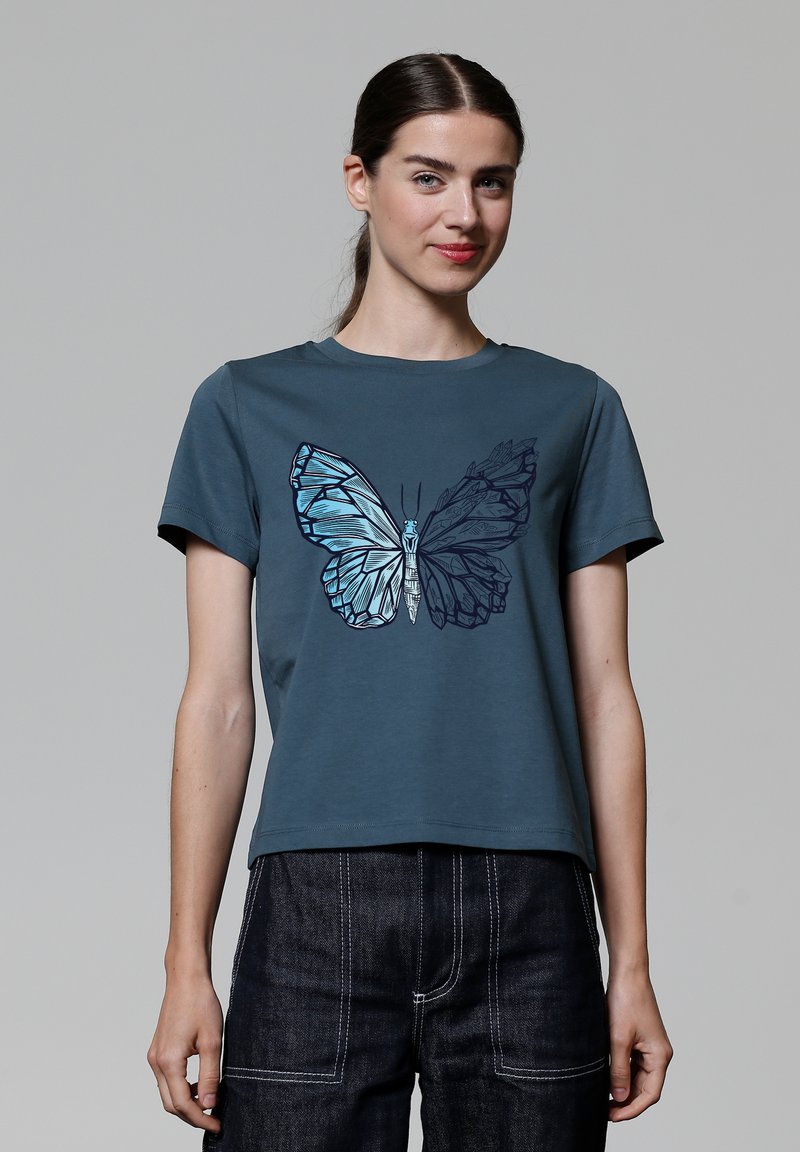 T-shirt en coton teal avec un graphique de papillon dans des nuances de bleu et noir. Manches courtes, col rond, coupe décontractée, texture lisse.
