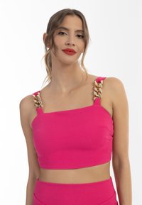 Top scurt roz, ajustat, cu decolteu pătrat, bretele groase și accente de lanț aurit pe umeri. Textură netedă și material elastic.