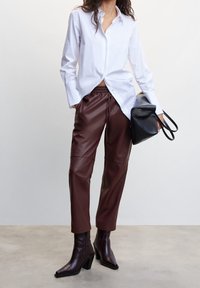White button-up shirt, brown faux leather pants, and dark heeled ankle boots. Bag is black with a smooth texture and structured design.