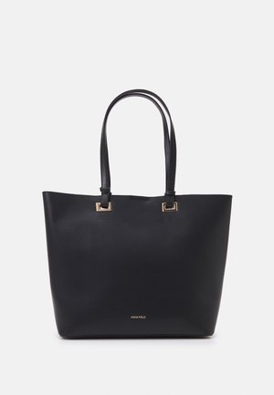 Sac cabas en cuir noir avec deux longues poignées et des accents en métal doré carrés, embossé d'un petit logo « Anna Field » au centre en bas.