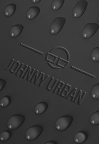 Tappetino in gomma nera con motivi a goccia d'acqua in rilievo e logo "JOHNNY URBAN" stampato, dalla consistenza liscia e dal design moderno.