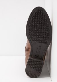 Botte en cuir marron avec semelle en caoutchouc. La semelle présente un motif texturé pour une meilleure adhérence. Détail d'une fermeture éclair latérale visible. Taille 37 marquée sur la semelle.