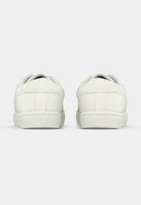 Ein Paar weiße Sneaker mit niedrigem Schnitt von hinten auf einem schlichten grauen Hintergrund gezeigt, wobei die sauberen Nähte und Gummisohlen hervorgehoben werden.