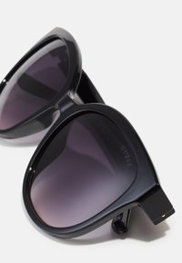 Black oversized sunglasses with gradient gray lenses, glossy plastic frame, and subtle brand logo on the arm. Features robust metal accents.
