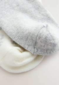 Par de calcetines: uno gris con un patrón texturizado y otro crema, ambos fabricados en un suave material de punto, mostrando un diseño de punta redondeada sencillo.