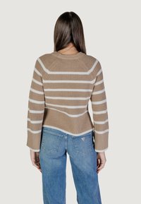 Maglione a righe marroni e crema con una texture a coste, maniche ampie e una vestibilità rilassata, abbinato a jeans in denim azzurro chiaro.