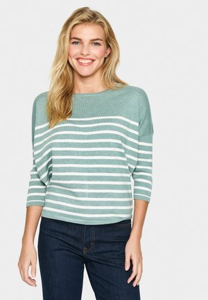 Lichtgroene gestreepte trui met wijde hals en driekwart mouwen, gecombineerd met donkere jeans; zachte textuur met een losse pasvorm.