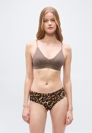 Γυναίκα με μακριά ξανθά μαλλιά που φοράει σουτιέν χρώματος ταφ και εσώρουχο με μοτίβο λεοπάρ, στέκεται μπροστά σε απλό φωτεινό γκρι φόντο.