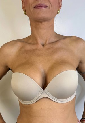 Sujeción sin tirantes color beige con tejido liso, copas moldeadas y diseño sin costuras. Presenta un cierre central y bordes curvados para un ajuste seguro.