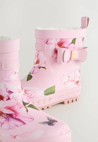 Bottes en caoutchouc roses avec un motif floral de fleurs de magnolia, une semelle texturée et un nœud décoratif sur le côté. Doublure douce visible.