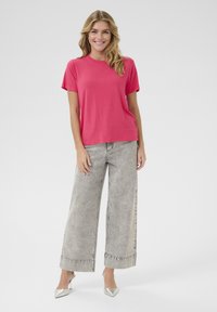 T-shirt rose à manches courtes et jeans large gris clair, avec des ourlets repliés et une texture lisse. Modèle portant des chaussures argentées.