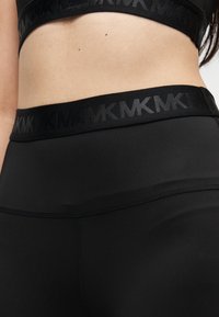 Musta urheilutrikoot, joissa leveä vyötärönauha kohokuvioidulla brändäyksellä, sileä pinta ja mukavuutta lisäävät litteät saumat.