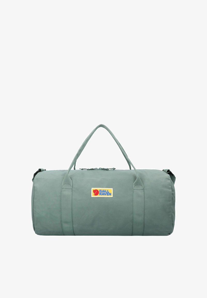 Sac de sport vert de forme ronde, fabriqué en tissu résistant. Il dispose de doubles poignées et arbore le logo Fjällräven en bleu et jaune.