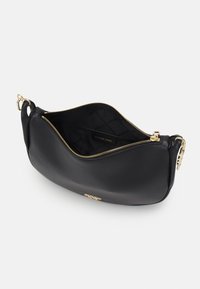 Czarna skórzana torebka na ramię Michael Kors z zamkiem, z detalami w kolorze złotym, częściowo otwarta, ukazująca pikowaną podszewkę i metkę marki.