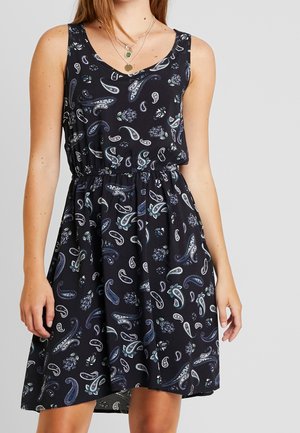 Czarna sukienka bez rękawów z niebiesko-białym wzorem paisley, z elastyczną talią, noszona z warstwowymi złotymi naszyjnikami.