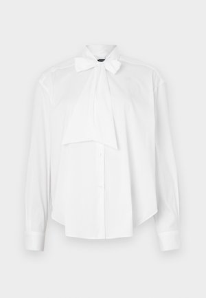 Blouse blanche à manches longues, col avec nœud, devant boutonné et coupe décontractée. Fabriquée en tissu lisse sans motifs ni accents.
