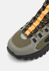 Green leather and mesh sneaker with black rubber sole, orange and black laces, and reflective gray accent. Features rugged design for stability.