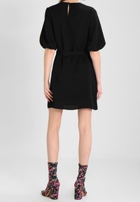 Černé krátké šaty s nabíranými rukávy, klíčovou dírkou na zádech a odpovídajícím opaskem. Nosit s botami po kotníky s květinovým vzorem a vysokými podpatky.