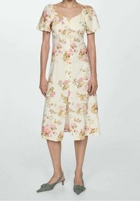 Robe florale en jaune clair avec des manches bouffantes courtes, bouton devant et longueur genou, ornée de motifs floraux roses et verts.