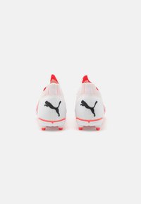 Scarpe da calcio bianche e rosa con una tomaia in mesh testurizzato. Presentano un logo Puma nero sul tallone e dettagli rossi sulla suola.