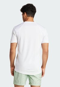 Camisa atlética blanca de manga corta con una textura suave. Cuenta con mangas raglán y un cuello redondo. Combinada con shorts de color verde claro con un patrón.