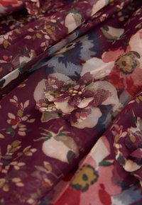 Ziedu mežģīņu audums burgundijas krāsā ar daudzkrāsainiem ziedu rakstiem, kas izceļ smalkas ziedlapas un caurspīdīgu, teksturētu virsmu.