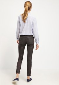 Camicia azzurro chiaro a righe con bottoni, jeans skinny neri con orli sfrangiati e scarpe slip-on blu scuro, viste da dietro.