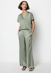 Completo in satin a due pezzi in verde pallido. Top a maniche corte con scollatura a V e pantaloni a gamba larga con elastico in vita e tasche laterali.