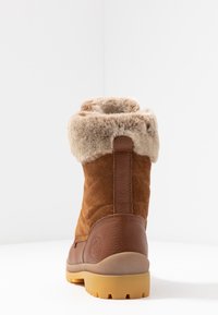 Botte en suède marron avec un revers en fausse fourrure, présentant une surface texturée, un bout arrondi et une semelle en caoutchouc avec une bande de roulement à motif.