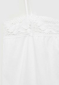 Camisole blanche avec un bord en dentelle sur le haut, des bretelles réglables et un tissu doux et texturé en dessous. Conception simple et légère.