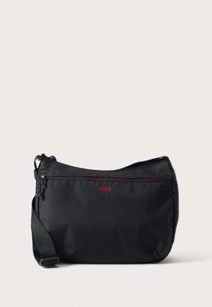 Zwarte crossbodytas met verstelbare band, voorvak met rits en rood "HUGO" logo op gladde stof.