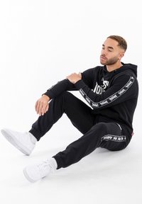 Sudadera con capucha y pantalones jogger de mezcla de algodón. Diseño con capucha y estampado gráfico. Los joggers tienen rayas laterales blancas y puños elásticos. Zapatillas blancas.