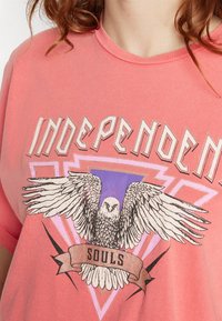 Pink cotton t-shirt featuring a graphic design with an eagle, text "INDEPENDENT" in bold lettering, and a banner with the word "SOULS."