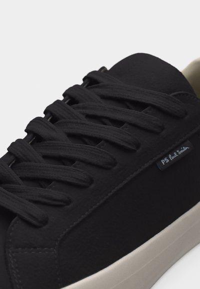 Baskets noires à lacets avec semelle blanche et petite étiquette "PS Paul Smith" sur le côté, présentées en vue rapprochée et en angle.