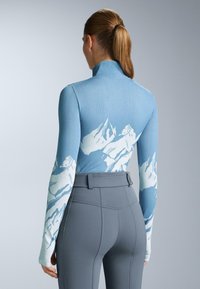 Dolgimi rokavi, svetlo modra majica z belim vzorcem gore; v kombinaciji z visokim pasom, oprijetimi sivo-črnimi legicami.