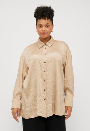 Chemise beige surdimensionnée à boutons avec une texture froissée, manches longues, col et boutons marron à l'avant.