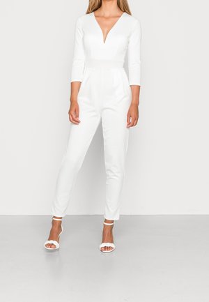 Witte jumpsuit met een diepe V-hals, driekwart mouwen, getailleerde taille en taps toelopende pijpen. Gekocht met witte hakken. Gladde textuur.